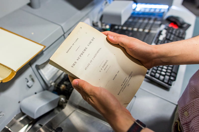 a technician holding disbound pages from a case reporter in front of a high speed scanner